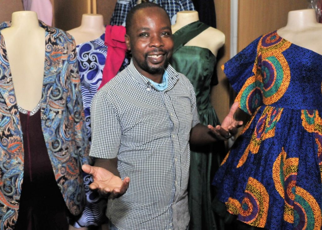 Sunninghill square | Johannesburg, Sandton, Mall, Shopping Centre, Convenient, Near Me, South African, Local, Affordable, Quality Sam The Tailor busy working on a dress, grey and black checkered shirt, holding hands in air